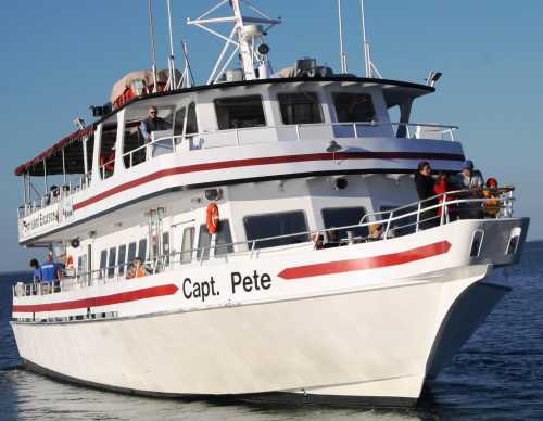 A large white boat named "Capt. Pete" with passengers on deck, sailing on calm waters under a clear blue sky.