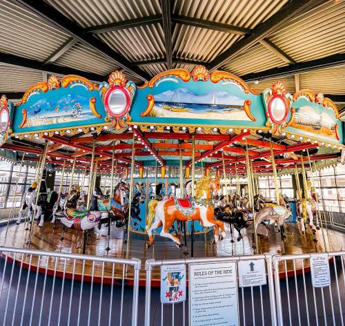 A colorful carousel with intricately painted horses, set under a metal roof in a bright, open space.