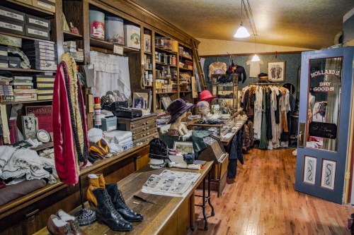 A vintage shop interior filled with clothing, hats, and various antique items on wooden shelves and tables.