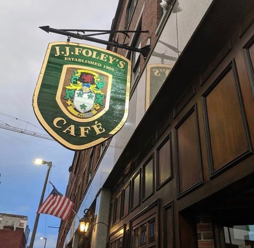Sign for J.J. Foley's Café, established in 1900, hanging outside a brick building with an American flag nearby.
