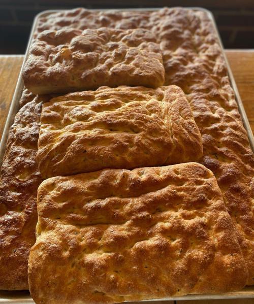 Freshly baked focaccia bread on a tray, featuring a golden-brown crust and a fluffy texture.