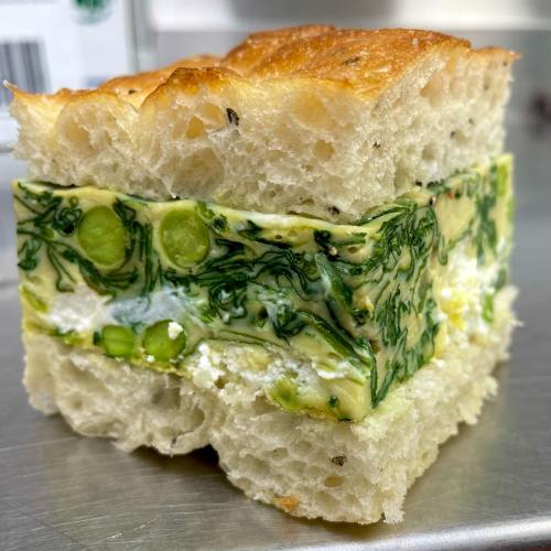A slice of focaccia bread layered with a green vegetable and cheese filling, showcasing vibrant colors and textures.