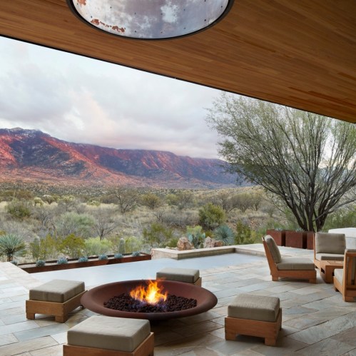 A modern outdoor space with a fire pit, seating, and a stunning view of mountains and desert landscape.