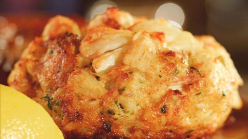 Close-up of a golden-brown crab cake with chunks of crab meat, served with a lemon wedge.