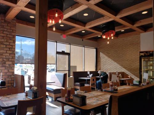 Interior of a cozy restaurant with wooden beams, booths, and large windows letting in natural light.