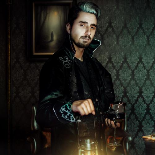 A man in a dark, ornate room wears a stylish coat and holds a glass, casting a mysterious aura.