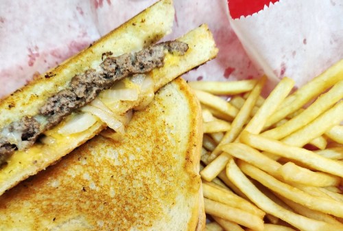A grilled cheese sandwich with ground beef and onions, served with a side of golden French fries.