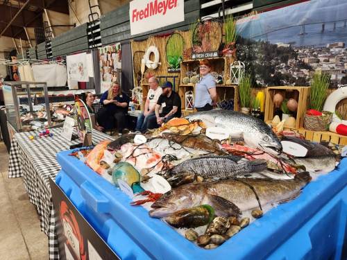 A seafood display at a market with various fish and shellfish, with people sitting in the background.