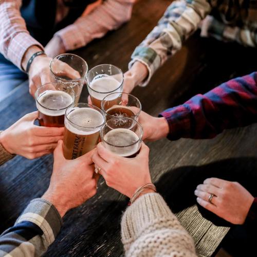 A group of hands toasting with various glasses of beer on a wooden table.