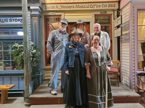 Five people in vintage clothing pose in front of a historical medical office, showcasing a 19th-century theme.