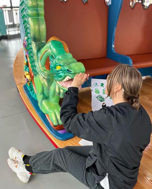 A person sits on the floor, coloring a green dragon figure on a carousel, surrounded by colorful decorations.