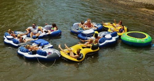 A group of people relaxes on colorful inner tubes in a river, enjoying a sunny day.