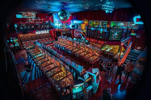 A vibrant arcade filled with pinball machines, skee-ball, and colorful lights, bustling with people enjoying games.