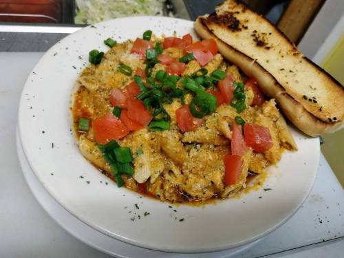 A plate of pasta topped with diced tomatoes and green onions, served with a slice of garlic bread on the side.