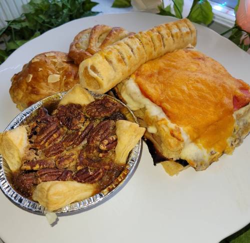 A plate featuring a slice of cheesy lasagna, a pecan pie, and two pastries, one with a twisted shape and the other round.