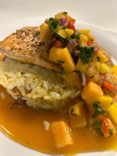 A plate featuring grilled salmon on a bed of rice, topped with a colorful mango salsa and a rich sauce.