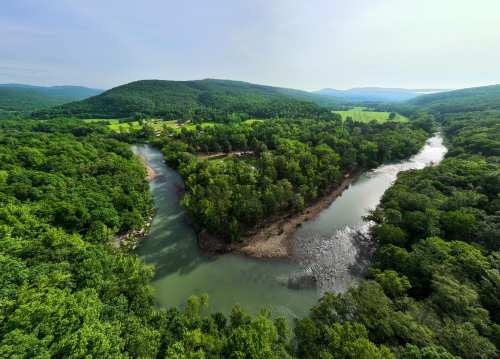 Aerial view of a winding river surrounded by lush green forests and rolling hills under a clear sky.