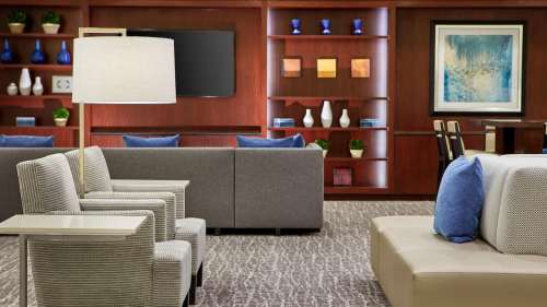 Modern lounge area with gray seating, decorative shelves, and a lamp, creating a cozy atmosphere.