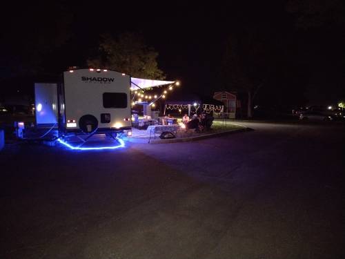A camper with blue lights at night, surrounded by a cozy outdoor setup and string lights in a campsite.