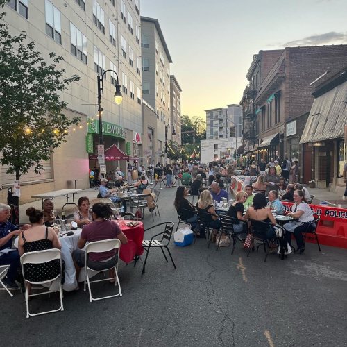 A lively street scene with people dining at tables, enjoying a community event as the sun sets.