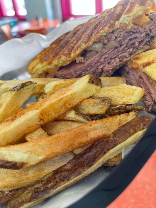 A close-up of a sandwich with layers of meat and onions, served with a side of golden, crispy French fries.