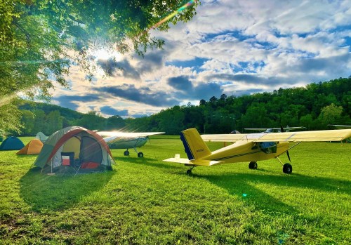 A yellow plane parked near tents on a grassy field, with trees and a cloudy sky in the background.