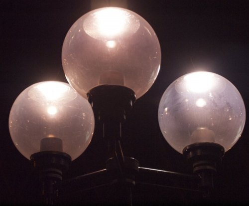 Three illuminated globe street lamps against a dark background, casting a warm glow.