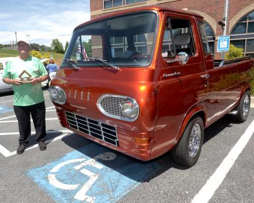 A person stands next to a vintage orange Ford pickup truck parked in a disabled parking space.