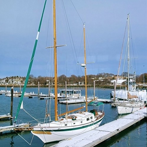 Two sailboats docked at a marina, with calm waters and a cloudy sky in the background.