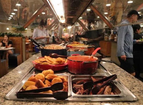 A buffet with various dishes, including meats, sides, and desserts, under a glass display in a restaurant setting.