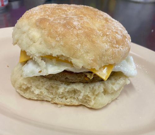 A biscuit sandwich with a fried egg, cheese, and sausage patty on a plate.