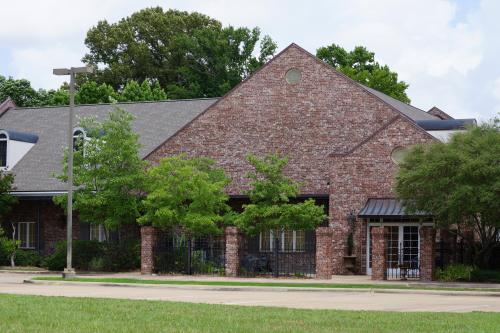 A brick building with large windows, surrounded by trees and a grassy area, under a partly cloudy sky.