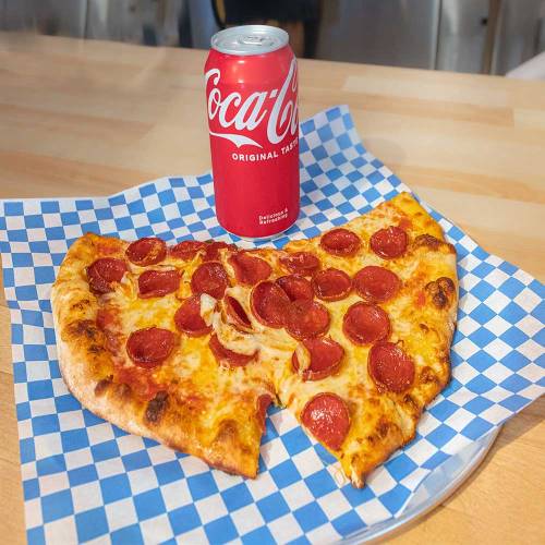 A slice of pepperoni pizza on a blue checkered paper plate next to a can of Coca-Cola.