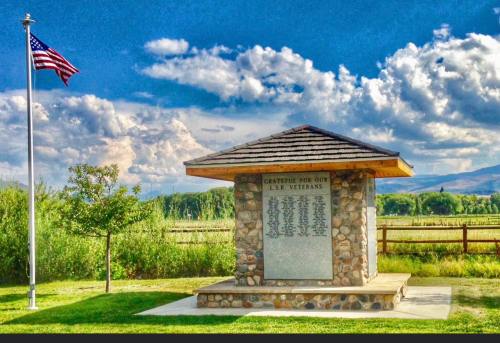 A stone monument honoring veterans, with a flagpole and a blue sky filled with clouds in the background.