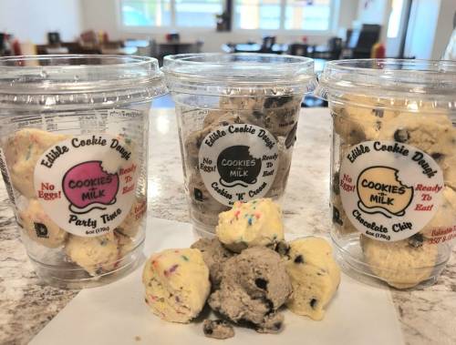 Three cups of edible cookie dough in flavors: Party Time, Cookies 'n' Milk, and Chocolate Chip, with dough balls in front.