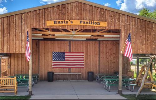 A wooden pavilion with "Rusty's Pavilion" sign, featuring an American flag and picnic tables underneath.