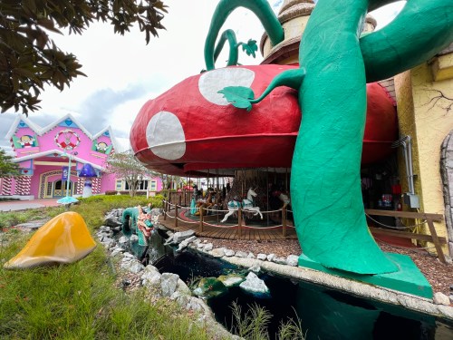 A whimsical structure resembling a giant mushroom, surrounded by colorful buildings and a small pond.