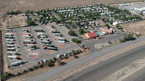 Aerial view of an RV park with numerous parked RVs, surrounded by trees and a building, near a highway.