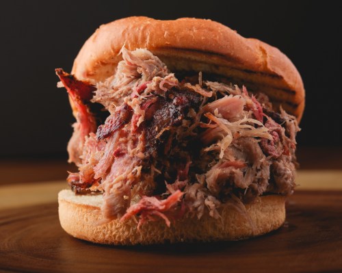 Close-up of a pulled pork sandwich with tender meat piled high on a soft bun.