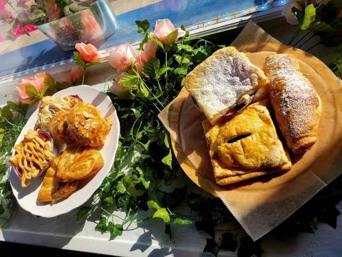 A plate of assorted pastries, including croissants and danishes, displayed with flowers and greenery in a bright setting.