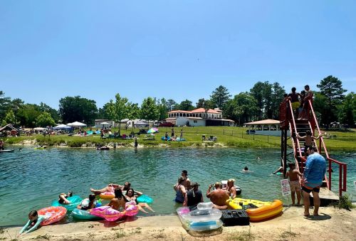 A sunny day at a swimming area with people on floats, a diving board, and a grassy shore in the background.