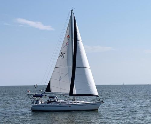 A sailboat with a white sail glides across calm waters under a clear blue sky.