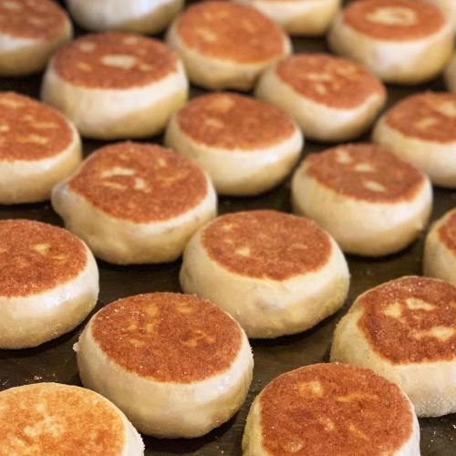 A close-up of freshly cooked English muffins, golden brown on top, arranged neatly on a baking tray.