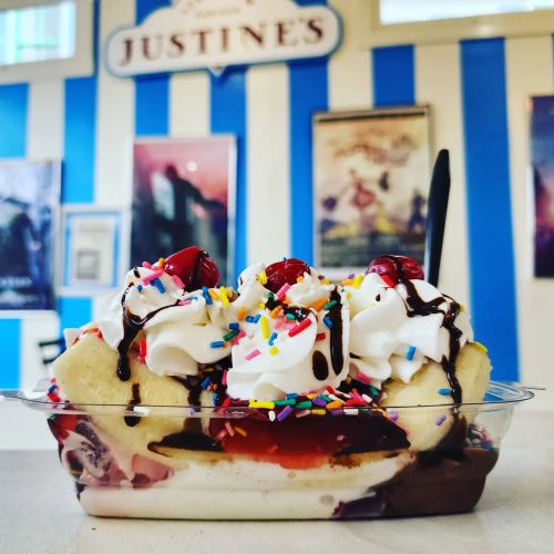 A colorful banana split topped with whipped cream, cherries, chocolate syrup, and sprinkles in a clear dish.