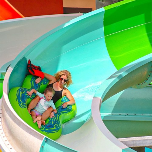 A woman and a child slide down a colorful water slide, enjoying a fun day at a water park.