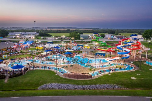 Aerial view of a vibrant water park with slides, pools, and crowds enjoying the evening atmosphere.