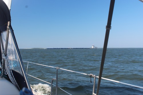 A view from a boat on the water, with a distant shoreline and a clear blue sky.