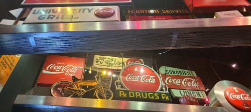 A collection of vintage signs, including Coca-Cola, a bicycle, and various advertisements, displayed in a vibrant setting.