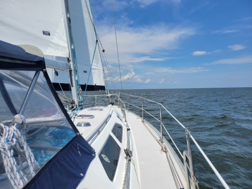 A sailboat glides over calm waters under a blue sky with scattered clouds.