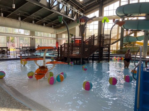 Indoor water park featuring colorful slides, a play structure, and beach balls floating in the pool.